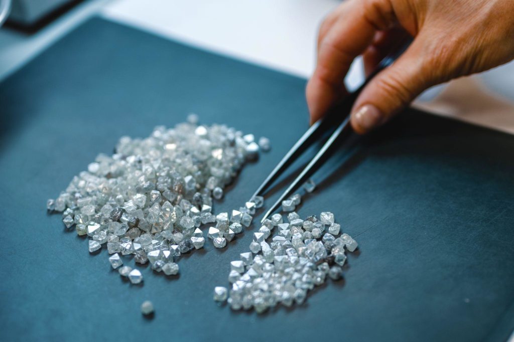 A hand with tweezers transfers diamonds from one pile to another