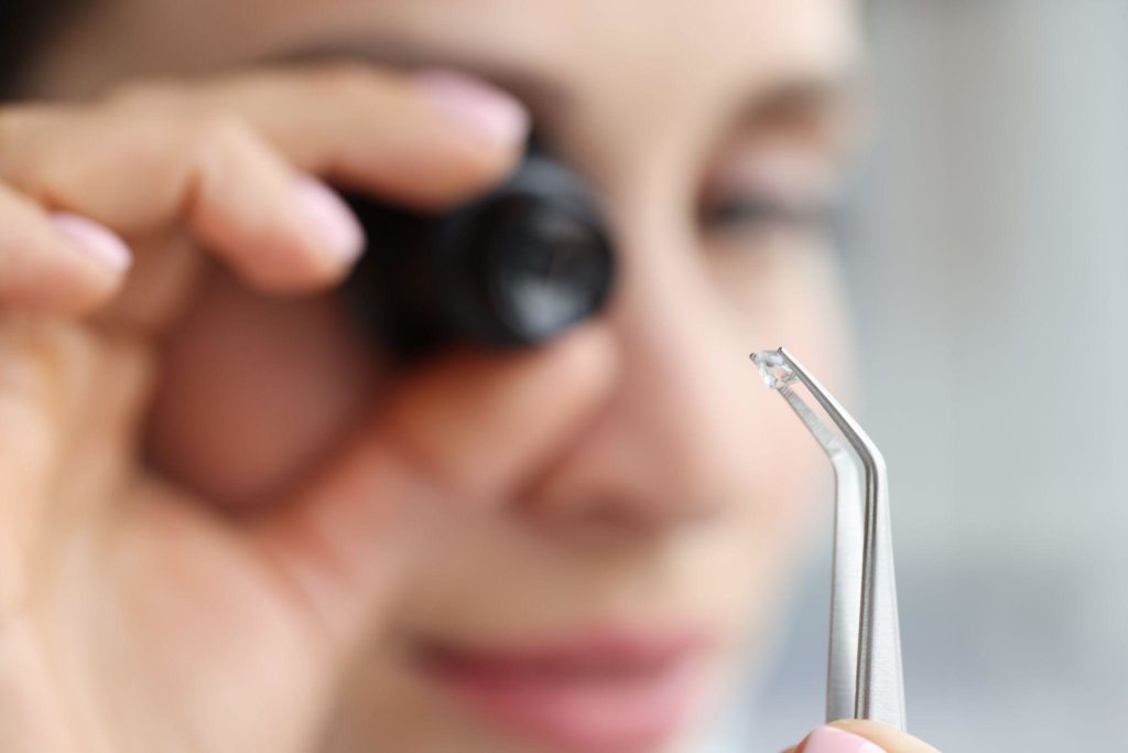 Jewelut looks through magnifying glass at gem in tweezers closeup