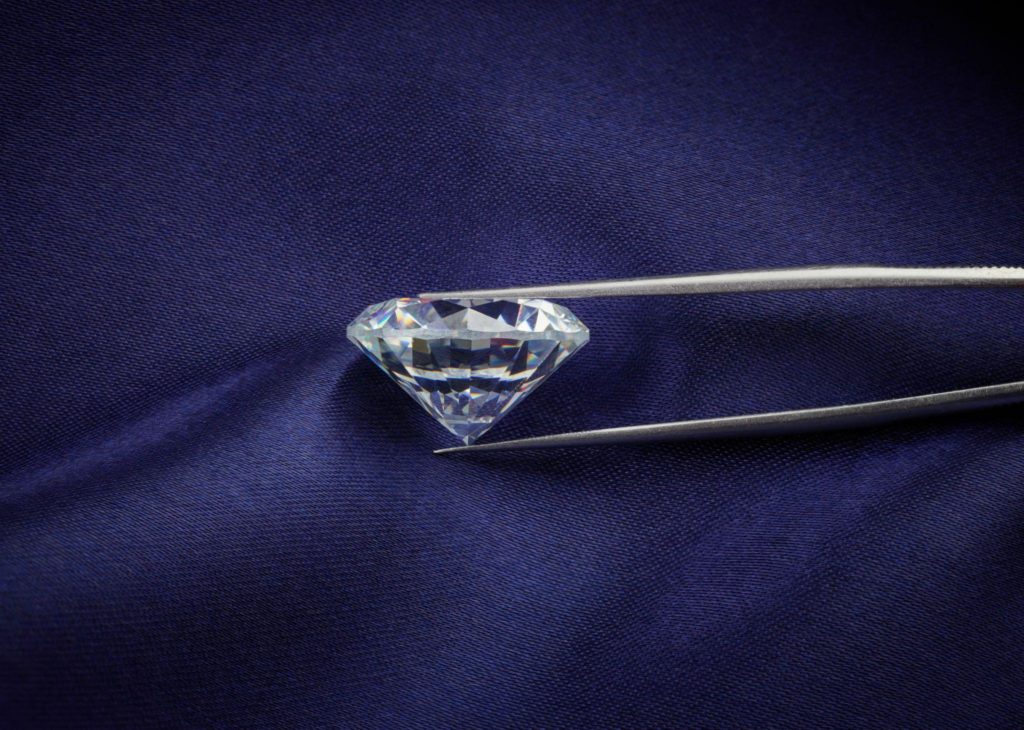 Diamond held in tweezers with light and reflection in facets.
