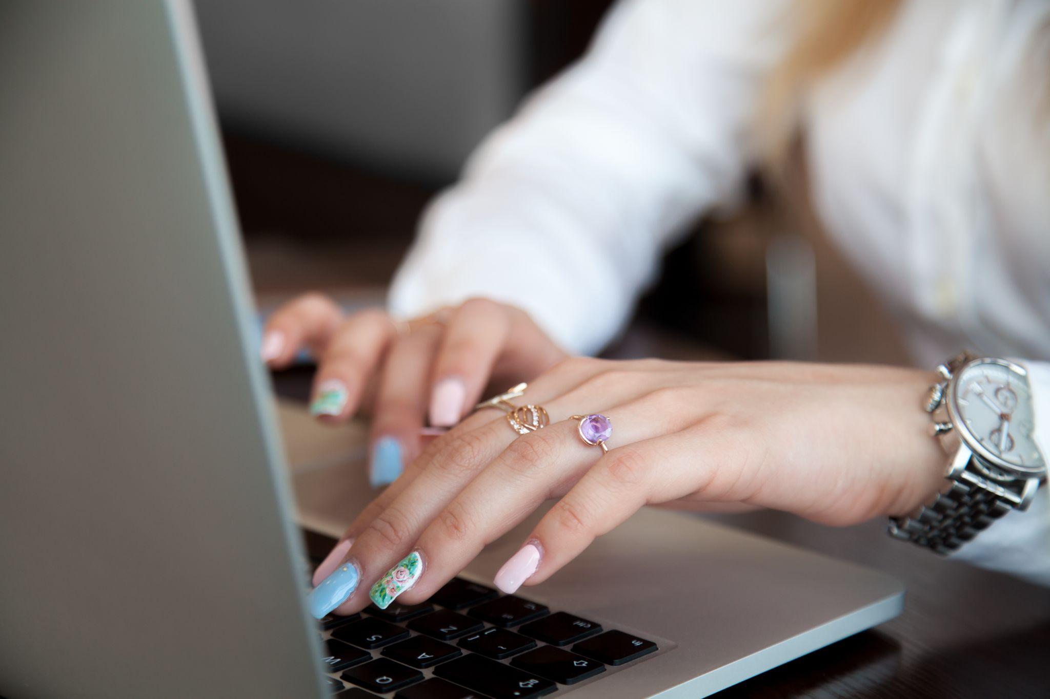Girl hands on laptop using touch pad and keyboard with rings on fingers and colorful manicure